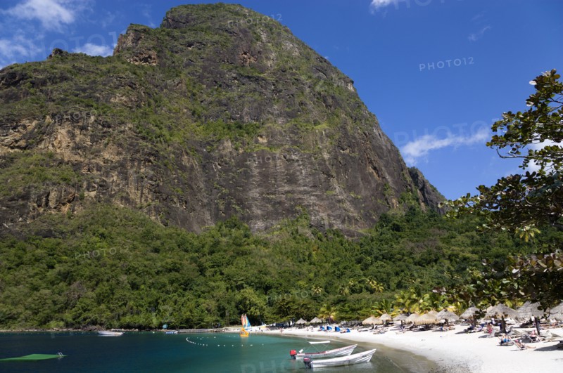 WEST INDIES, St Lucia, Soufriere , Val des Pitons The white sand beach at the Jalousie Plantation Resort Hotel with the volcanic plug of Petit Piton beyond and tourists on sunbeds beneath palapa sun shades