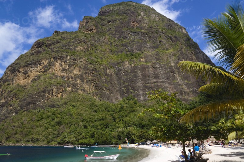 WEST INDIES, St Lucia, Soufriere , Val des Pitons The white sand beach at the Jalousie Plantation Resort Hotel with the volcanic plug of Petit Piton beyond and tourists on sunbeds beneath palapa sun shades
