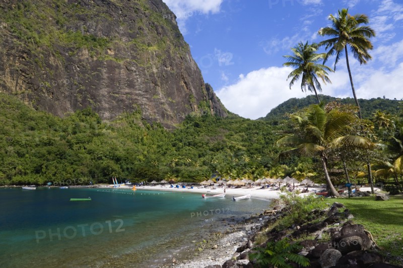 WEST INDIES, St Lucia, Soufriere , Val des Pitons The white sand beach at the Jalousie Plantation Resort Hotel with the volcanic plug of Petit Piton beyond and tourists on sunbeds beneath palapa sun shades