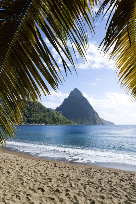 WEST INDIES, St Lucia, Soufriere, Soufriere Beach lined with coconut palm trees with the town and the volcanic plug mountain of Petit Piton beyond