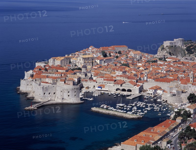 CROATIA, Dalmatia, Dubrovnik, Elevated view over the Old City Harbour with fortified walls. Yachts moored in marina surrounded by buildings with terracotta tiled rooftops