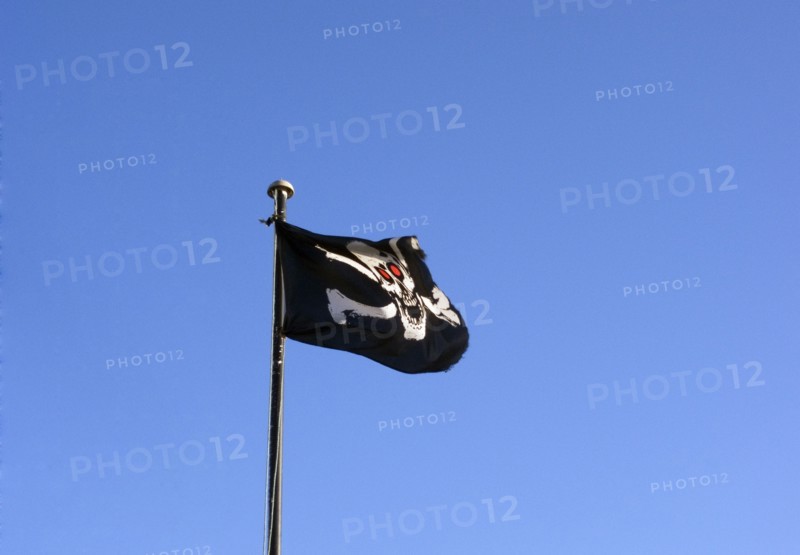 ENGLAND, East Sussex, Hastings, Skull and cross bones pirate flag flying against a blue sky