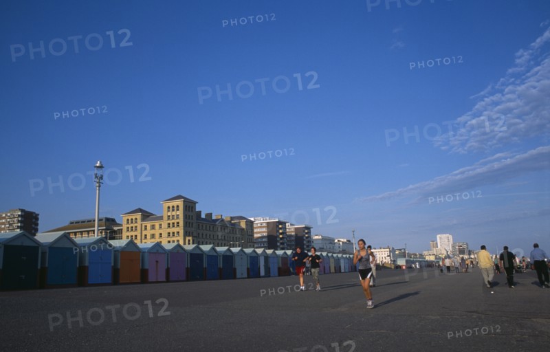 ENGLAND, East Sussex, Brighton, Joggers on Hove Lawns Esplanade by colourful beach huts in late afternoon sunshine.