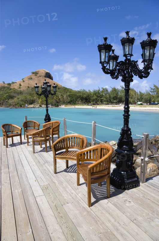 WEST INDIES, St Lucia, Gros Islet , Signal Hill on Pigeon Island National Historic Park seen from a nearby wooden jetty with a table and chairs beside a wrought iron lamppost