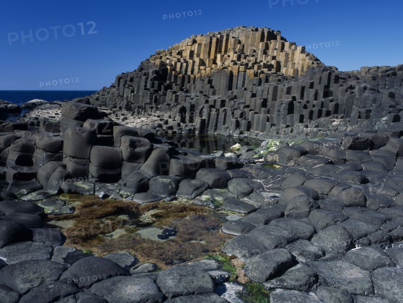 NORTHERN IRELAND, County Antrim, Giants Causeway, Interlocking basalt stone columns left by volcanic eruptions. View across the main and most visited section of the causeway with the coastline seen behind.