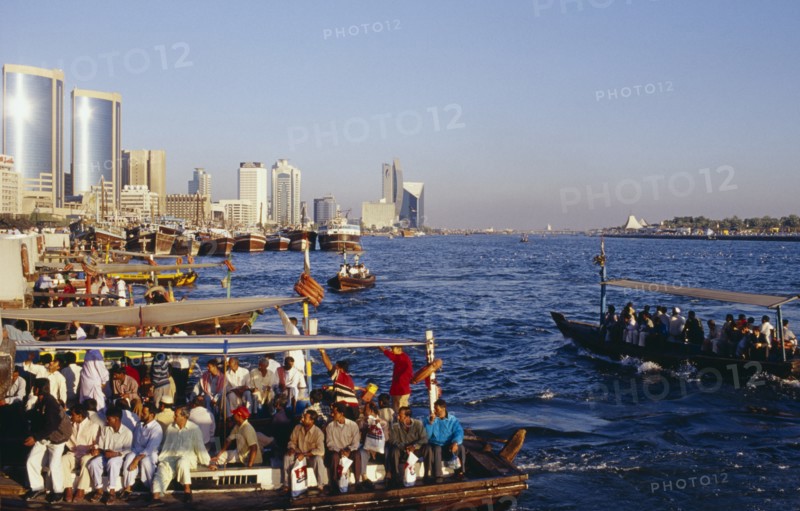 UAE, Dubai, Dubai Creek, Abra water taxis with passengers on Creek with city skyline beyond.