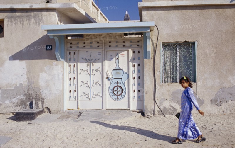 UAE, Dubai, Bur Dubai , Young girl passing building with carved and decorated doorway.  Sheikh Zayed Road behind.