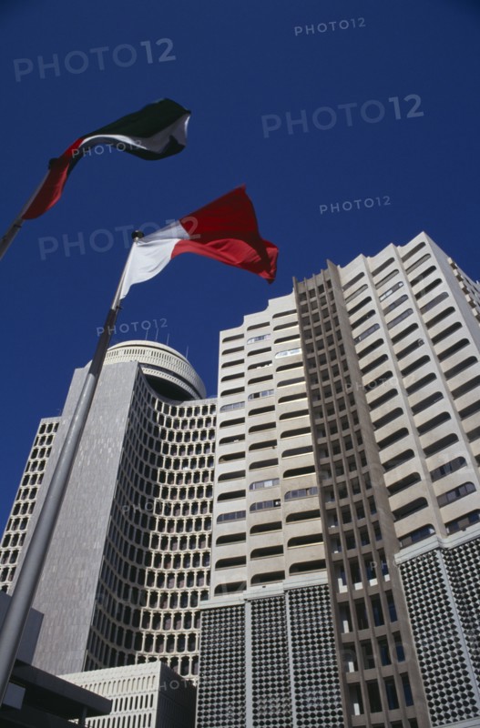 UAE, Dubai , Deira Tower.  Looking up at high rise building with flags flying in foreground.