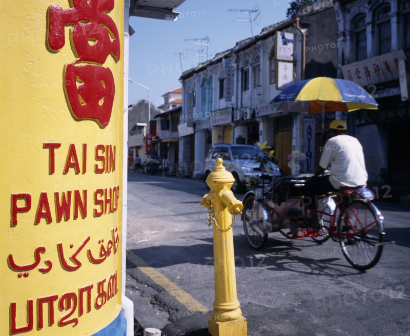 MALAYSIA, Penang, Georgetown, Lebuh Chulia.  Cycle rickshaw on street with yellow and red painted sign for pawn shop written in four different languages in immediate foreground.