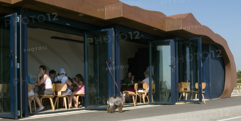 ENGLAND, West Sussex, Littlehampton, Customers sitting at tables inside the East Beach Cafe designed by Thomas Heatherwick. Dog tied to glass door waiting outside