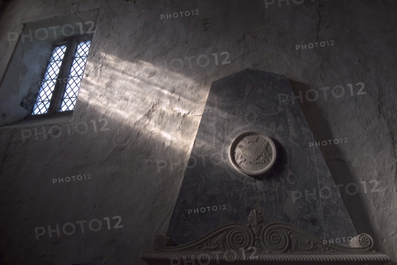 ENGLAND, West Sussex, Boxgrove, Boxgrove Priory Church of St Mary and St Blaise. Interior view of  light shining through small window onto a wall and marble monument.
