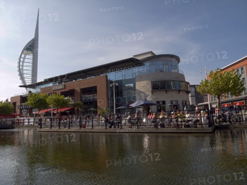 ENGLAND, Hampshire, Portsmouth, "Gunwharf Quays complex. View across water towards restaurants, bars and shopping outlets. Spinnaker Tower behind."