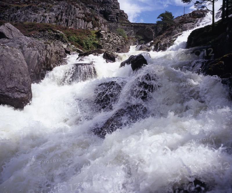 WALES, Gwynedd, Snowdonia National Park, Ogwen Falls and Nant Ffrancon Pass.   White foaming water tumbling over rocks with arched stone bridge in background.