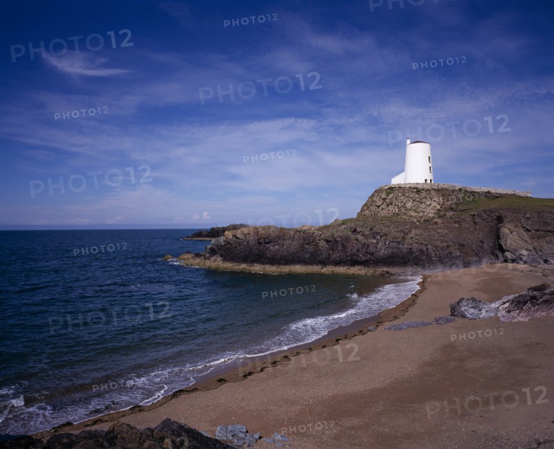WALES, Isle of Anglesey, Llanddwyn Island, "Curving, empty beach overlooked by old lighthouse standing on rocks extending out to sea.  Blue sky and windswept clouds above."
