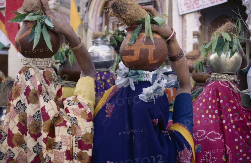 INDIA, Madhya Pradesh, Orccha, Back view of crowd of women carrying metal and earthenware pots on their heads with offerings of coconuts.