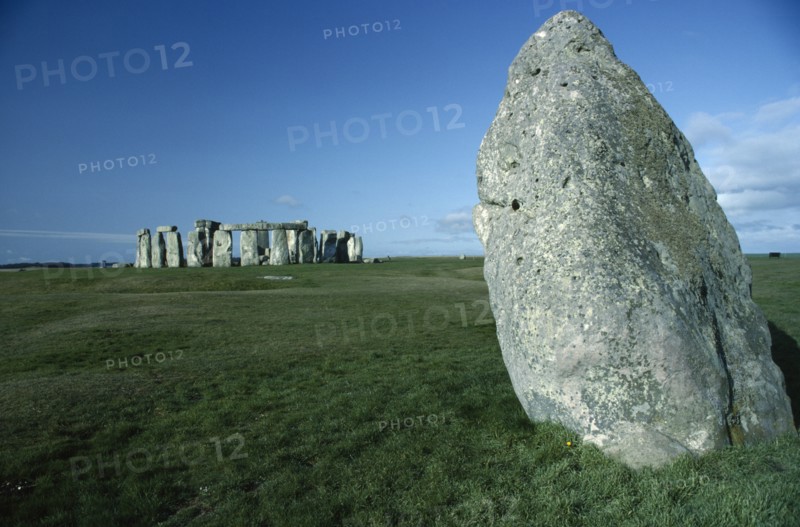 ENGLAND, Wiltshire, Stonehenge, View across the grass on Salisbury Plain toward the standing stones with a large stone in the foreground