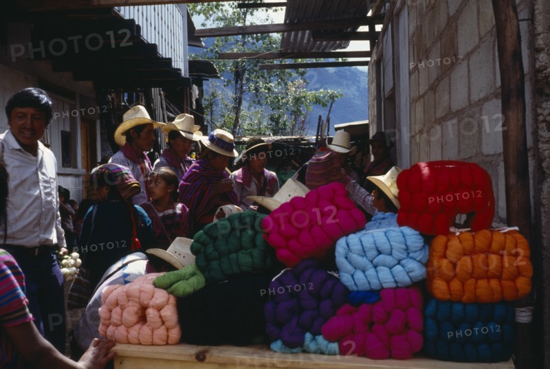 GUATEMALA, Todos Santos, Market scene with wool stall piled with brightly coloured bundles of wool and crowd of customers wearing traditional dress.