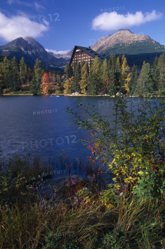 SLOVAKIA, Carpathian Mtns, High Tatras Mtns, Strbske Pleso.  View across lake towards chalet and mountains beyond with surrounding trees and vegetation in Autumn colours.