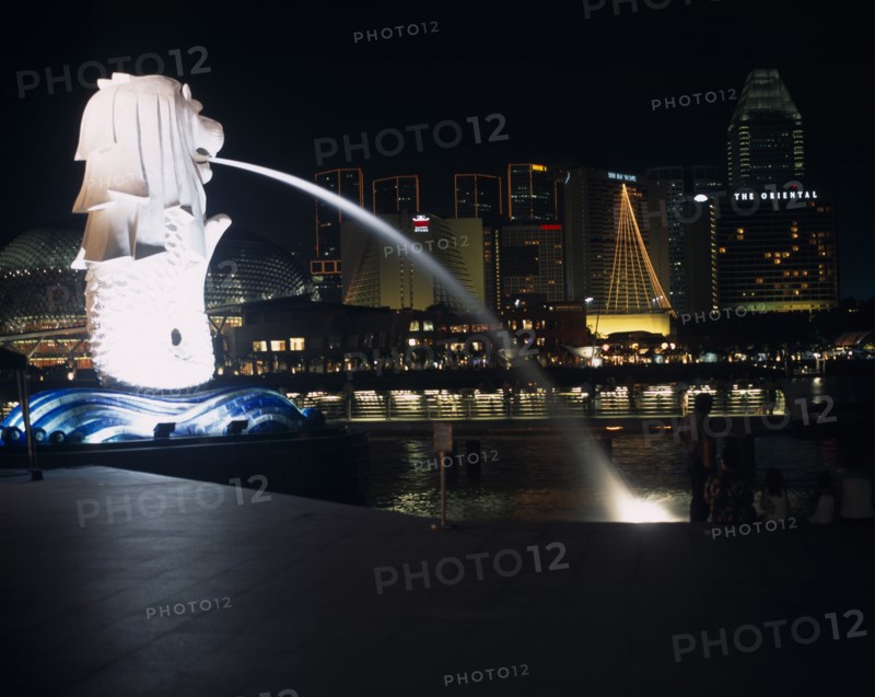 SINGAPORE, Merlion Park, "The Merlion statue at the Merlion Park river entrance at night with the esplanade concert hall, Oriental Hotel and other city buildings illuminated behind."