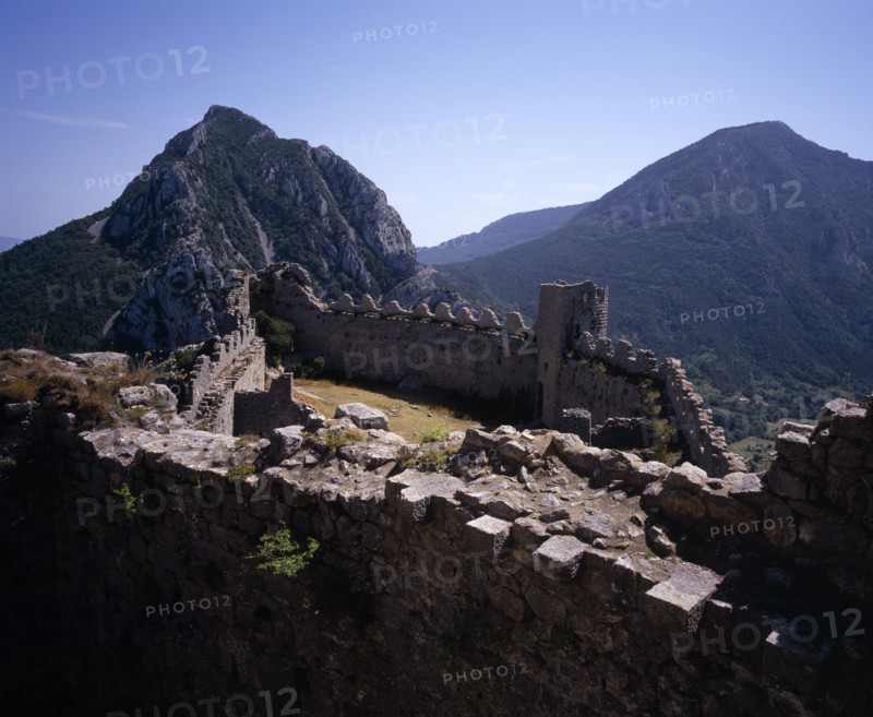 FRANCE, Languedoc-Roussillon, Aude, Chateau Puilarens.  Ruined medieval Cathar castle stronghold set high on limestone cliff.  View looking down on battlements from the keep to mountain peaks beyond.