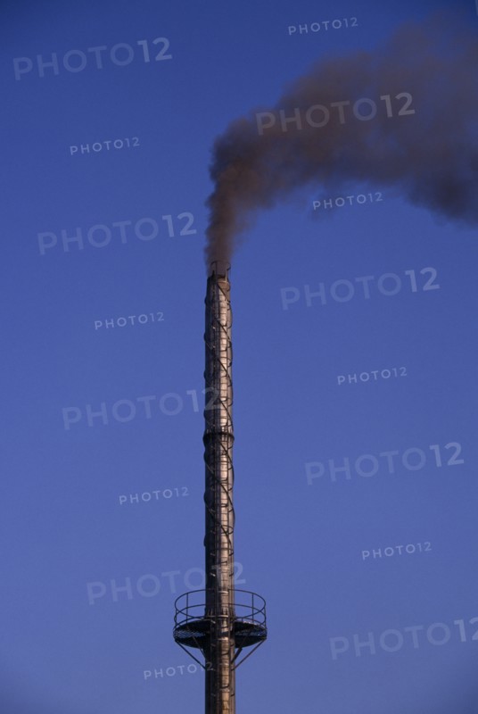 INDIA, Madhya Pradesh, Bhopal, Tall factory chimney emitting black smoke against blue sky.