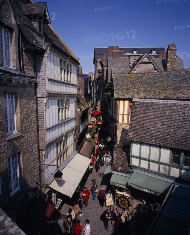 FRANCE, Normandy, Mont-St-Michel, "Looking down on narrow street, souvenir arcade and shoppers from outer wall footway."