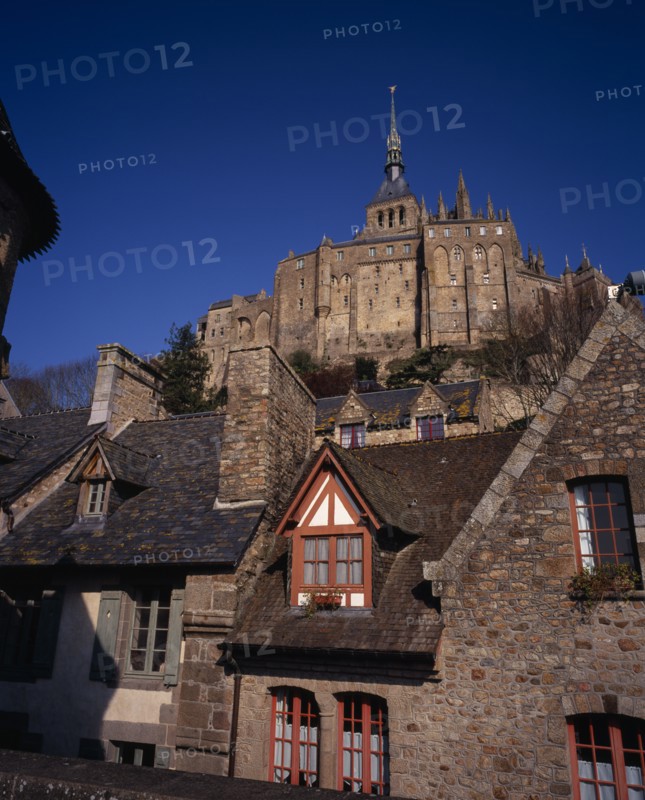 FRANCE, Normandy, Mont-St-Michel, The Abbey on hilltop above tiled rooftops of town houses from the Archade Tower.
