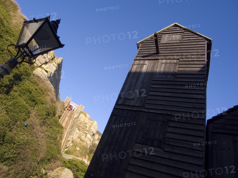 ENGLAND, East Sussex, Hastings, Black wooden huts used for storing fishing nets.The East Hill Lift funicular railway behind.