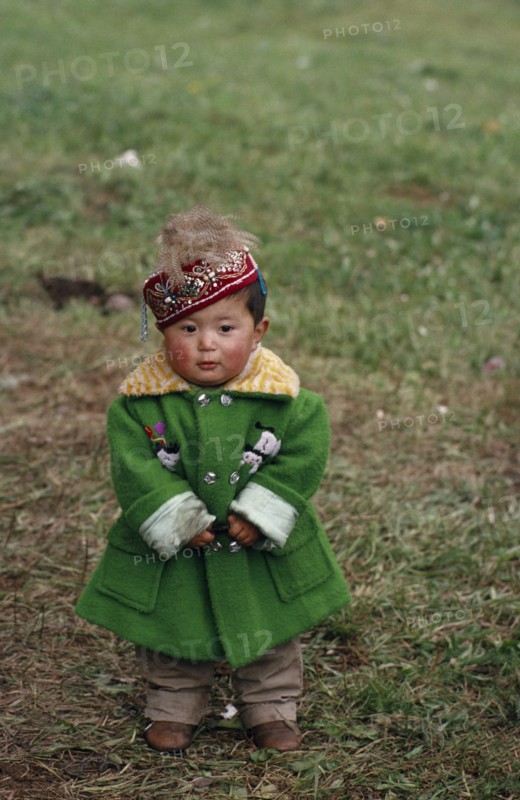 CHINA, Children, Portrait of young Kazakh child wearing green wool coat and embroidered cap.