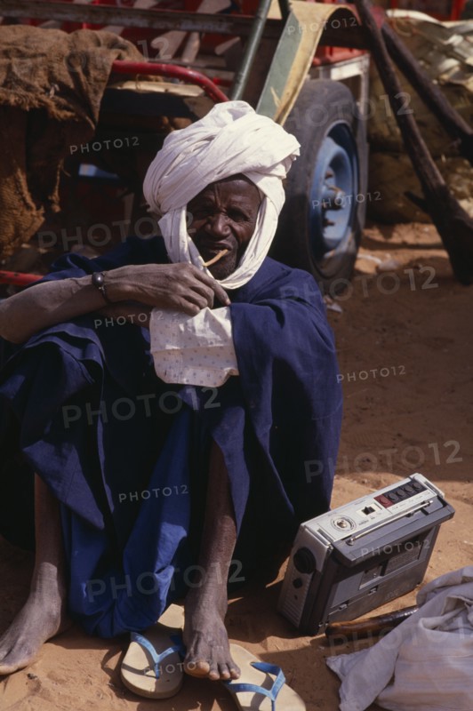SENEGAL, People, Portrait of Senegalese man seated on ground listening to radio.