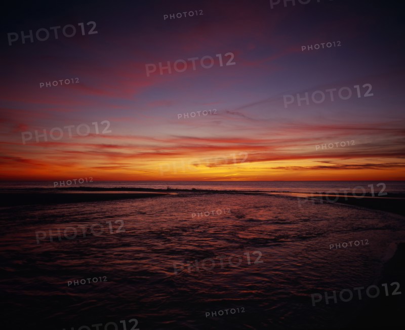 FRANCE, Aquitaine, Landes, Cap de L’Homy.  Red and orange sunset sky over Atlantic coastline with windswept clouds and rippled water surface.