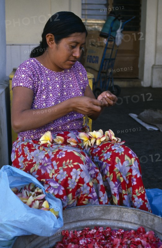 MEXICO, Juchitan, Woman in floral patterned skirt threading flower heads into garland at Juchitan street market.