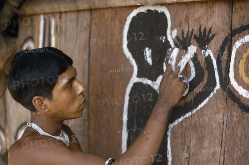 COLOMBIA, North West Amazon, Tukano Indigenous Tribe, Barasana man (sub group of Tukano) paints front of maloca large communal home. The symbolic shamanic figure is to keep evil spirits and bad weather away.