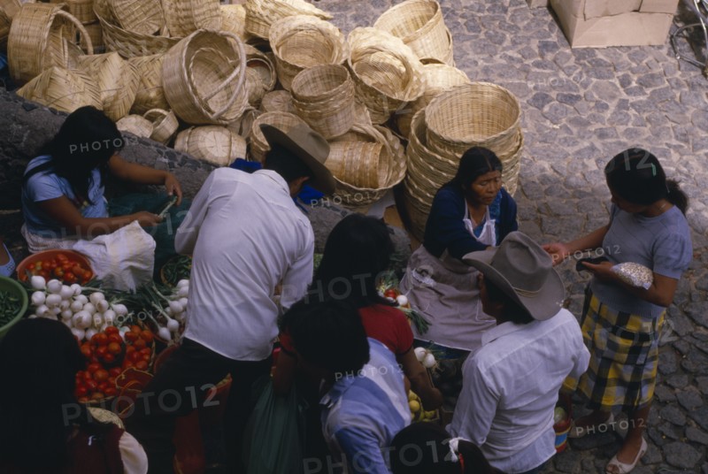 MEXICO, Taxco, Looking down on customers at fruit and vegetable stall in market with piled baskets behind.