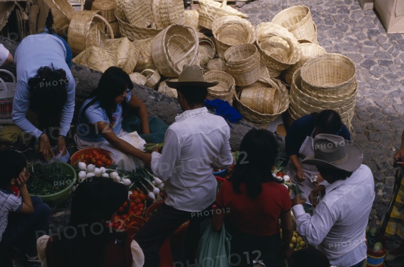 MEXICO, Taxco, Looking down on customers at fruit and vegetable stall in market with woven baskets piled behind.