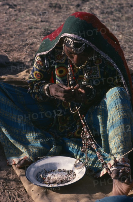 INDIA, Rajasthan, People, Kalbelia gypsy woman in traditional dress stringing beads.