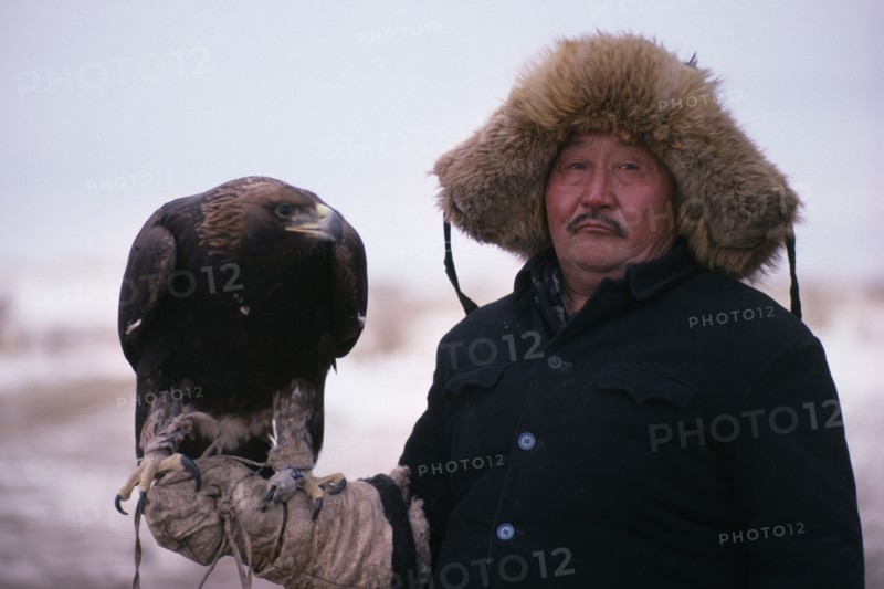 20088819 CHINA Xinjiang Province People Kazakh man wearing thick  fur lined hat and holding eagle on his gloved hand.