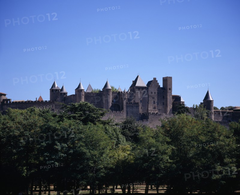 FRANCE, Languedoc-Roussillon, Aude, Carcassonne.  City view from west towards medieval fortified outer walls of old town and the chateau of the Count of Carcassonne with trees in the foreground.