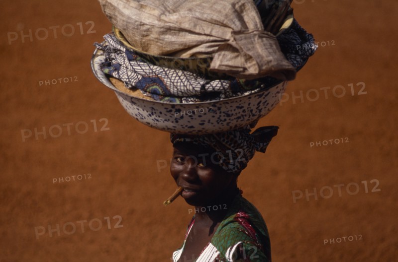 20088675 CENTRAL AFRICAN REPUBLIC  People Woman on her way to market carrying laden bowls on her head and chewing on a teeth cleaning stick.