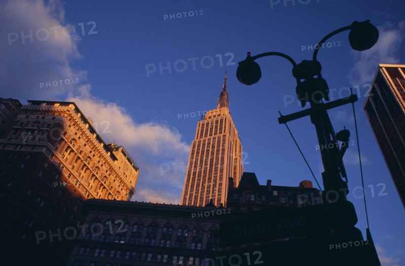 USA, New York, New York City, "Part view of the Empire State Building from 7th Avenue / West 31st Street in orange sunlight with silhouetted street light and buildings in deep shadow in foreground.   Designed by architect William Lamb of Shreve, Lamb and Harmon Associates.  Art Deco, steel framed with radio and TV mast completed in 1931."