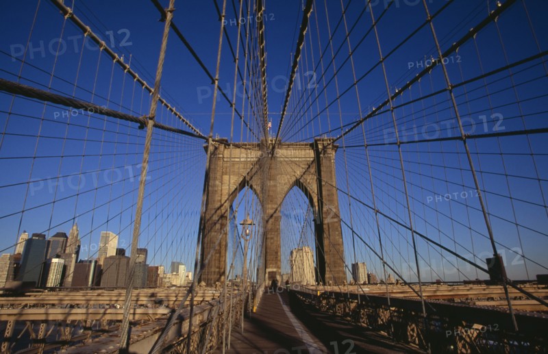 USA, New York, New York City, Brooklyn Bridge.  View along bridge to pedestrians at far end and Manhattan skyline beyond intersected by steel wires and suspension cables.