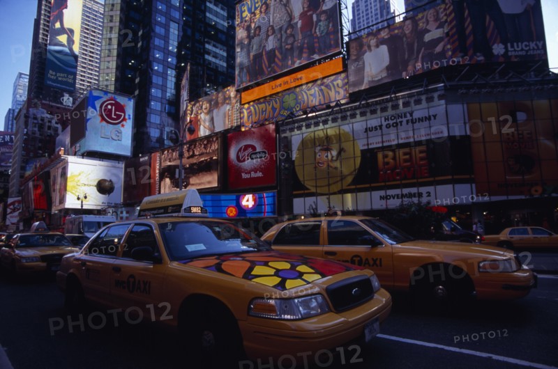 USA, New York, New York City, Times Square.  Yellow taxi cabs on street lined with skyscraper buildings and illuminated advertising in low light.