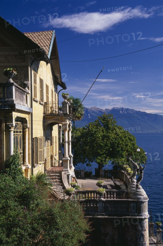 ITALY, Lake Maggiore, Part view of yellow painted exterior facade of villa with stone balustrade overlooking lake.