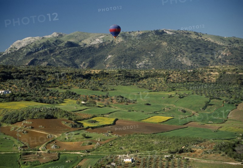 SPAIN, Andalucia, Malaga , A hot air balloon flying over green valley with patchwork fields towards mountain range