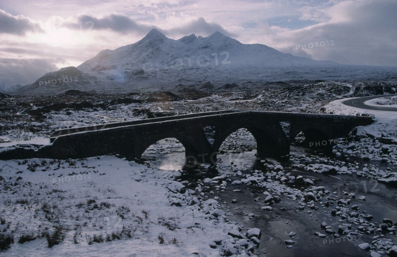 SCOTLAND, Isle of Skye, Sligachan and the Cuillin Mountains in winter snow.  Narrow bridge over frozen river and grey sky.