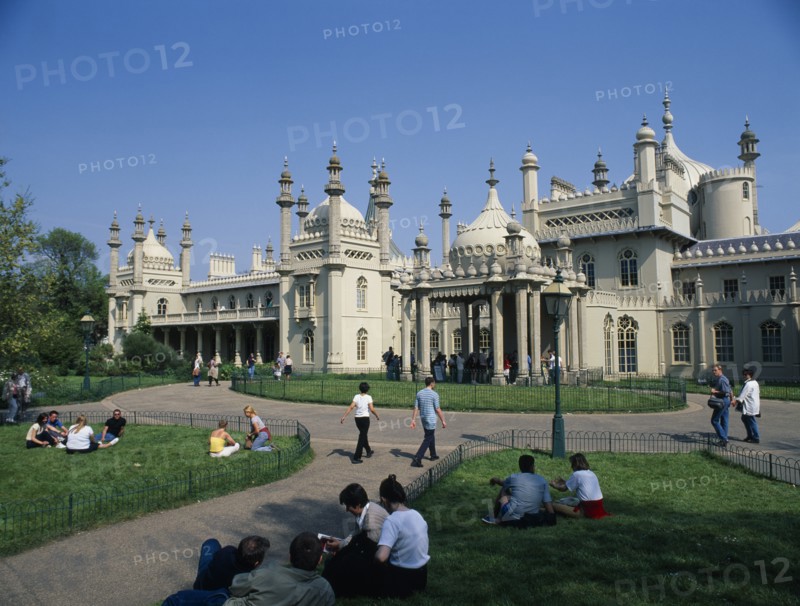ENGLAND, East Sussex, Brighton, The Royal Pavilion seen from the gardens with visitors at entrance and sitting on the grass