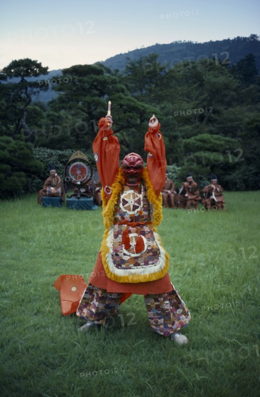 JAPAN, Customs, Dance, "Figure in mask and costume performing Genroku, a bugaku dance originating in India and coming to Japan via China in the eigth century.  Depicts a snake-eater hunting for his food.  Line of musicians behind."