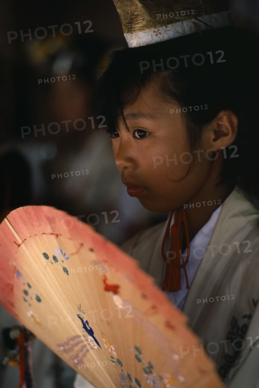 JAPAN, Kyushu, Kaseda Shrine, "Portrait of young shrine maiden employed to welcome visitors, supervise offerings and perform sacred dances for the Shinto gods or kami.  Head and shoulders, three-quarter portrait to left, carrying painted fan."