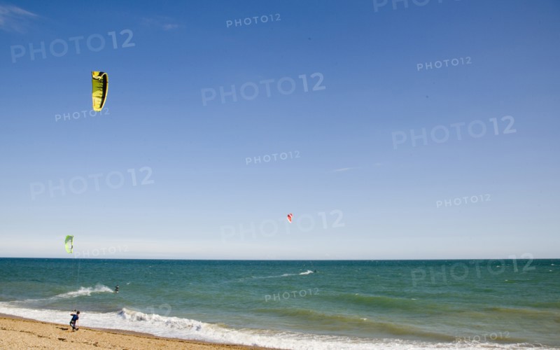 ENGLAND, West Sussex, Lancing, Kite Surfers on sea next to shingle beach in the summer with blue sky
