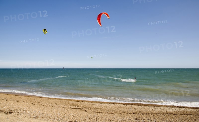 ENGLAND, West Sussex, Lancing, Kite Surfers on sea next to shingle beach in the summer with blue sky